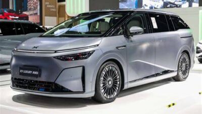 Silver multi-purpose vehicle on a showroom floor, front three-quarter view with large alloy wheels and slim LED headlights.