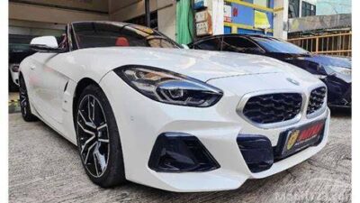 Front-left view of a white BMW sports car parked on a concrete city street, with large kidney grille and black alloy wheels visible behind the wheel