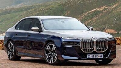 Blue BMW 7 Series luxury sedan parked on a scenic mountain road with green hills in the background.