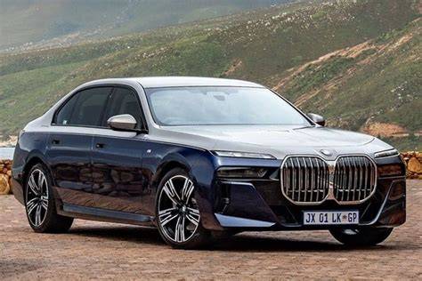 Blue BMW 7 Series luxury sedan parked on a scenic mountain road with green hills in the background.